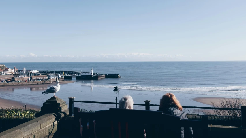 two people sitting on a bench overlooking the beach