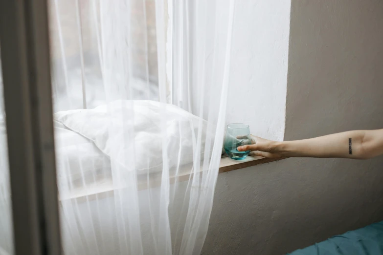 a persons hand resting on a glass in front of a window