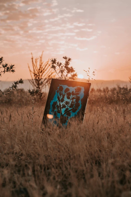 the sun sets behind an easel that has been placed in the middle of a field