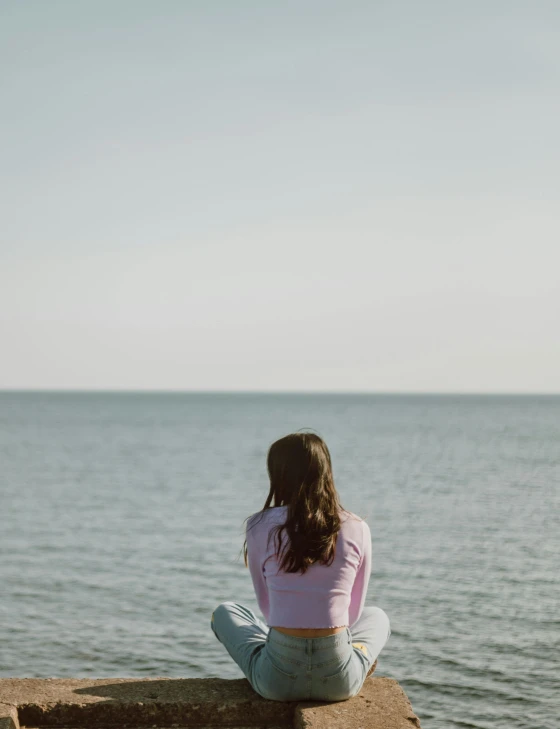 a girl sits on the rocks and looks out to the ocean