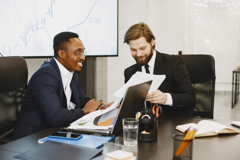 two men in business suits look at documents at a conference table