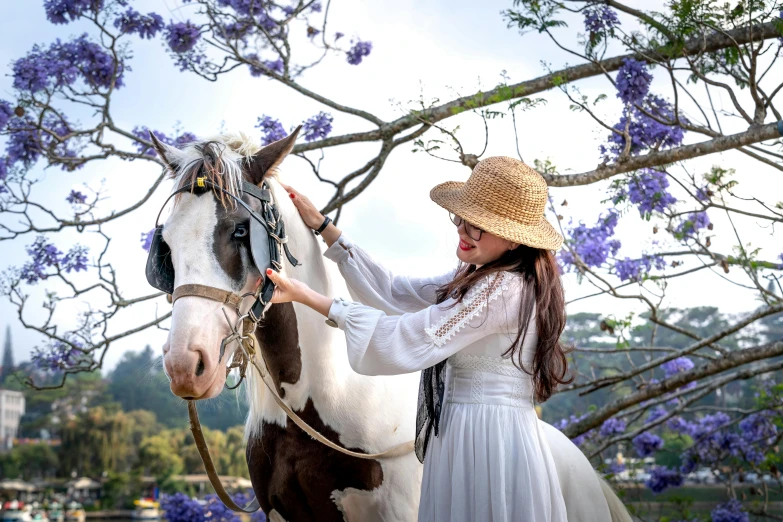 a woman in a dress and cowboy hat petting a pony