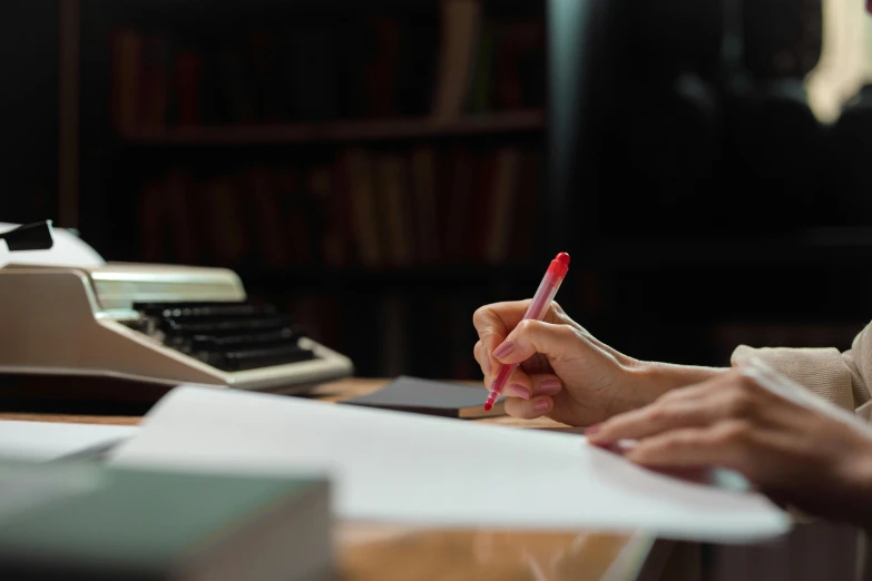 a person writing on paper while sitting in a chair with a typewriter and an old fashioned telephone