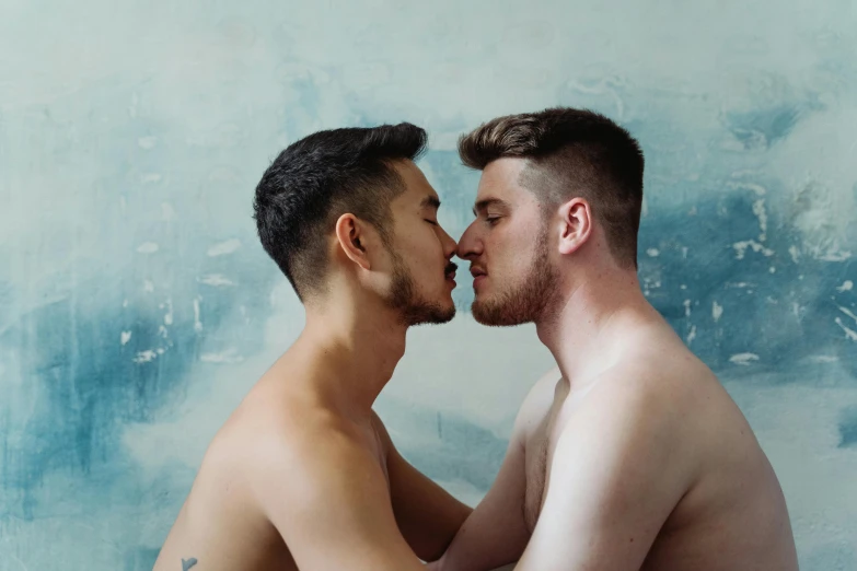 two gay men share a tender kiss in front of a blue wall