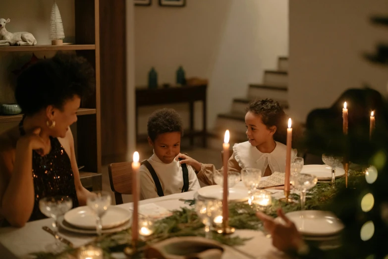 children are sitting around a table and candles glow in the background