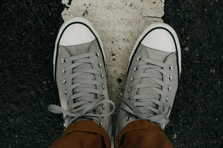 a person wearing gray sneakers standing next to asphalt