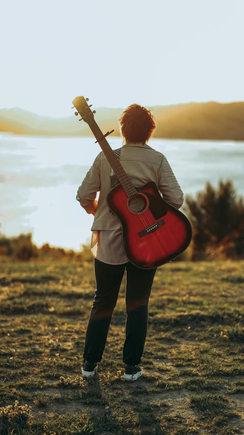 a person with a red guitar is standing next to the ocean