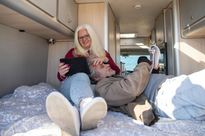 a man and woman sitting in the bed of an rv, one with a tablet computer
