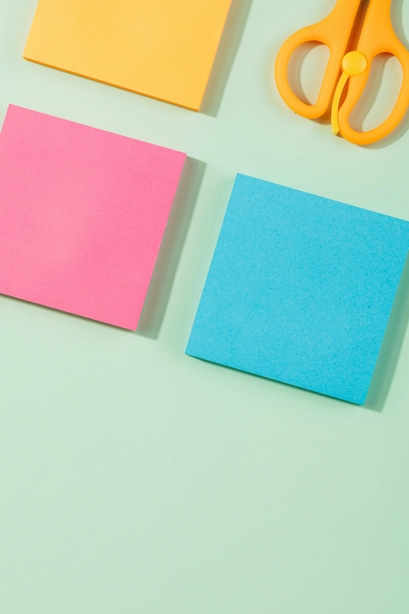 two sheets of paper with scissors, pink and blue paper on a light green background