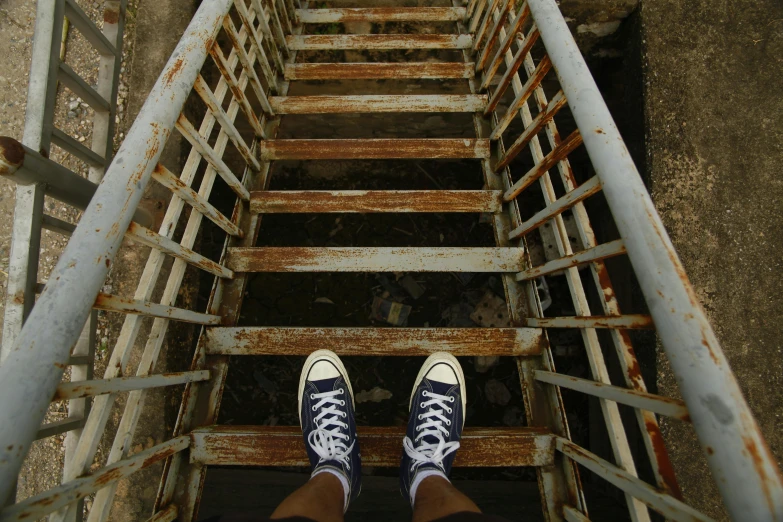 a person in tennis shoes standing on a rusty metal staircase
