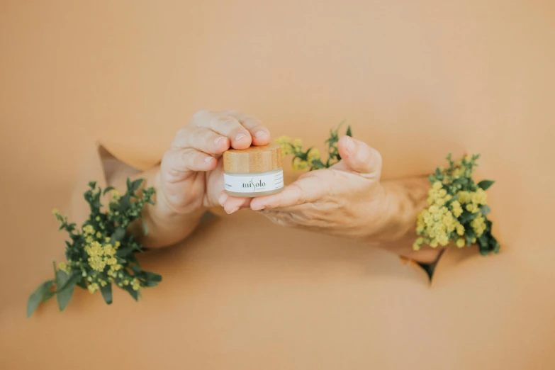 two hands are holding a small pill in front of a bunch of flowers