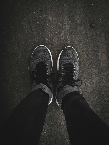 a person wearing sneakers looking down while standing on asphalt