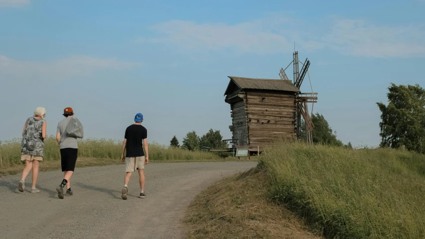 three men walking down a dirt road past a windmill