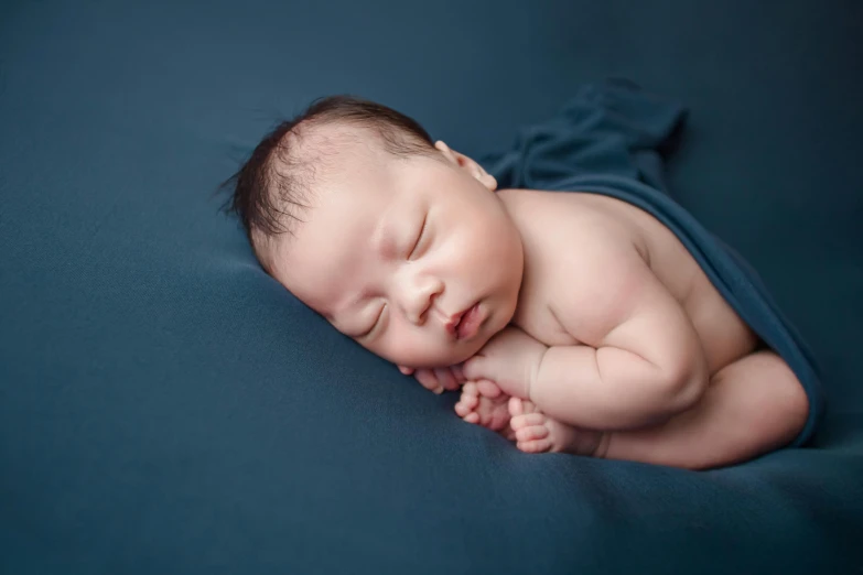 a baby laying on its side sleeping on blue fabric