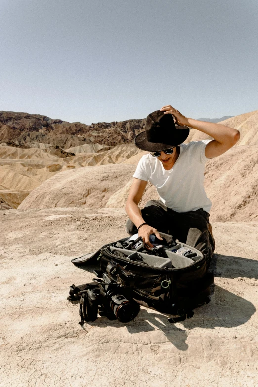 a man kneeling in the desert with a black suitcase