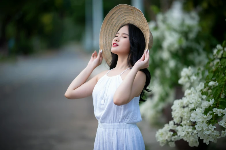 an asian woman in a white dress with hat by flowers