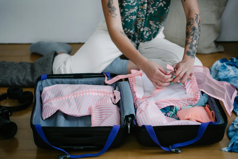 a woman with tattoos sitting on a floor next to a suitcase filled with clothing