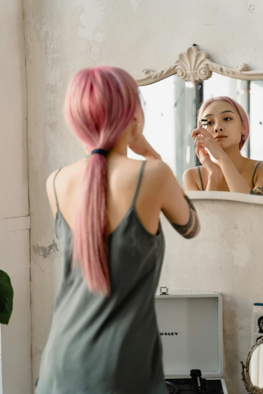 woman in grey tank top applying makeup in front of mirror