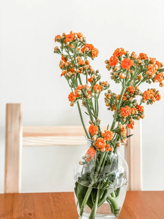 some orange flowers are in a clear vase on a wooden table