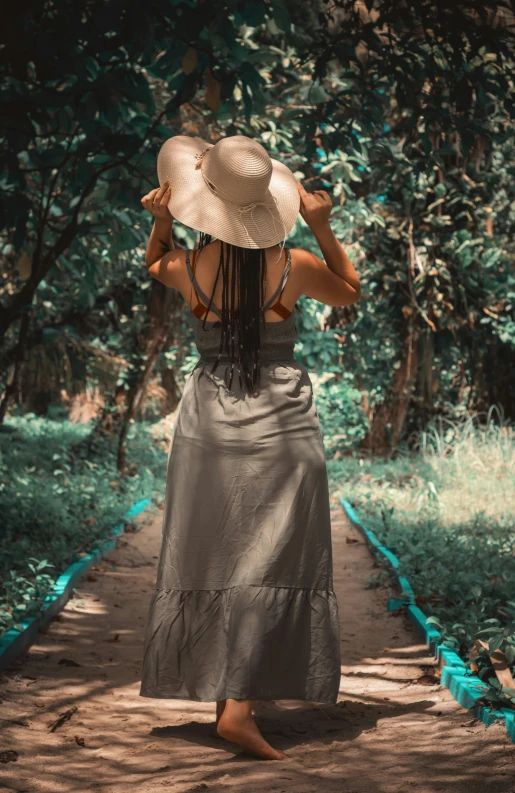 a woman walking down a dirt path wearing a white hat