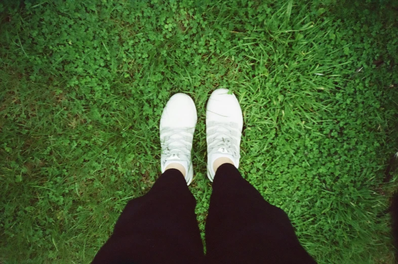 a person wearing white tennis shoes stands on grass