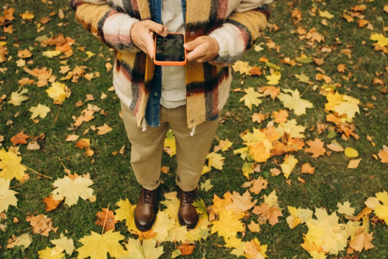 man in plaid scarf taking picture on leaf covered lawn