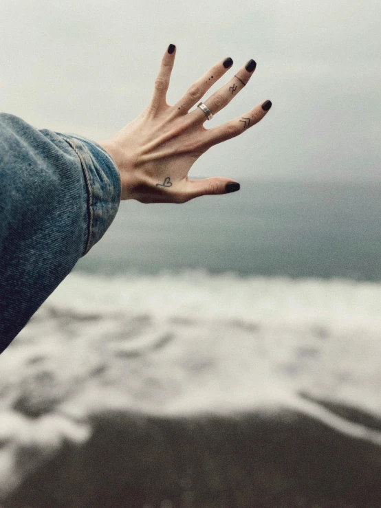 hand with black nails holding a beach background