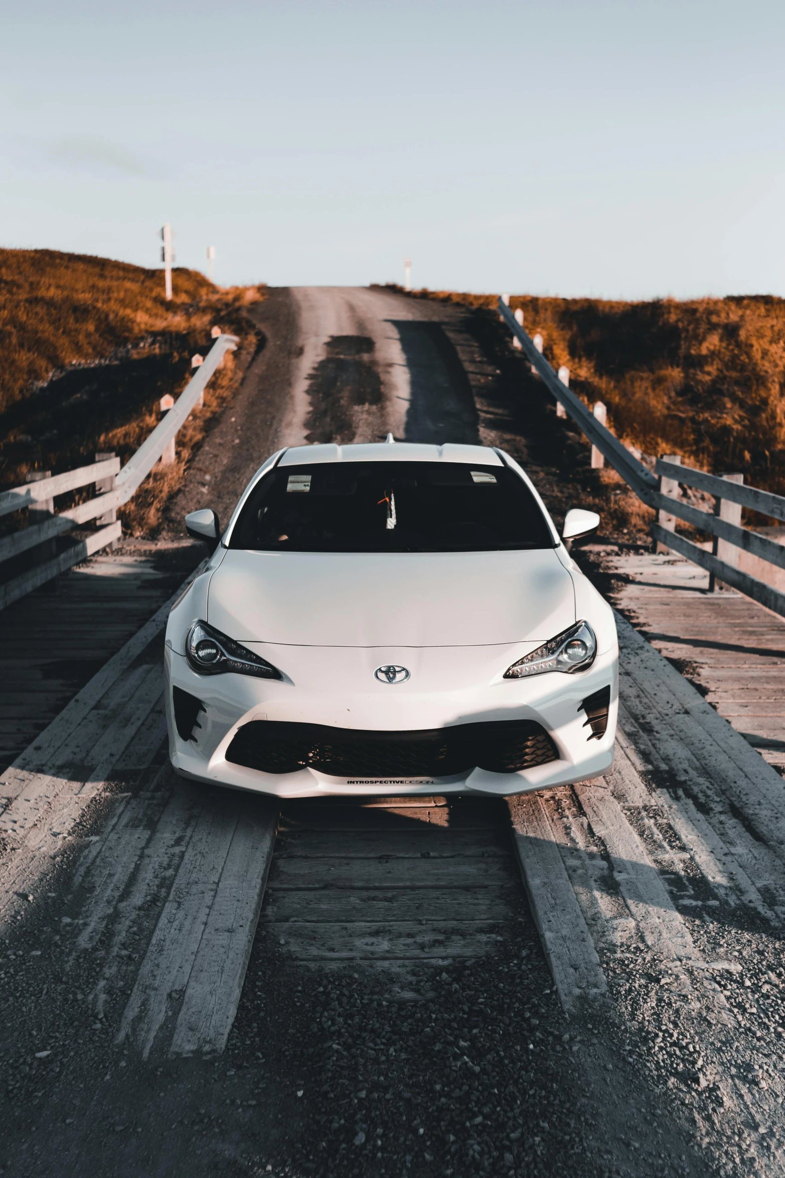 white sports car parked on the road with wooden fence