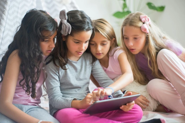 several girls look at an electronic device in a bedroom