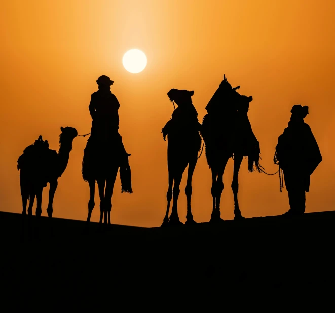 four people on camels with the sun setting in the distance