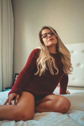 a beautiful woman sitting on top of a bed in glasses
