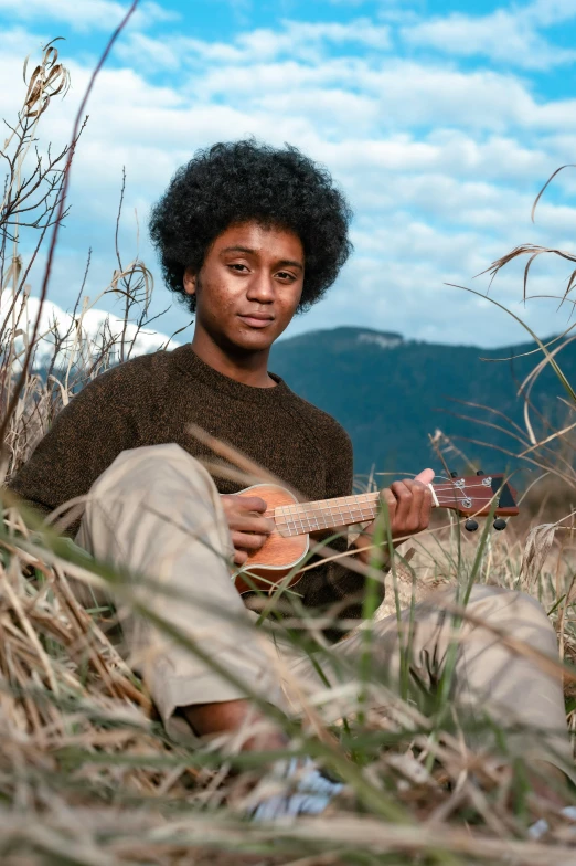 a young black man sitting in a wheatfield playing an acoustic guitar