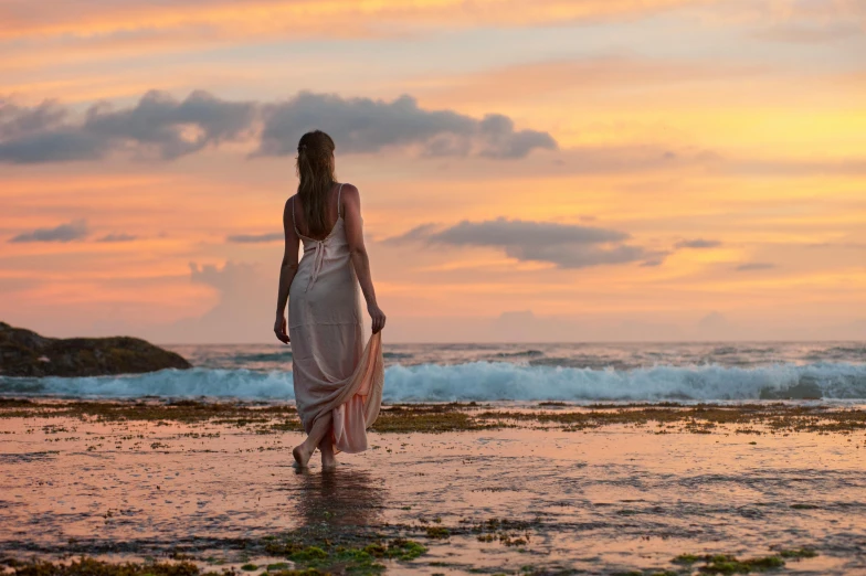 a woman walking on the beach at sunset