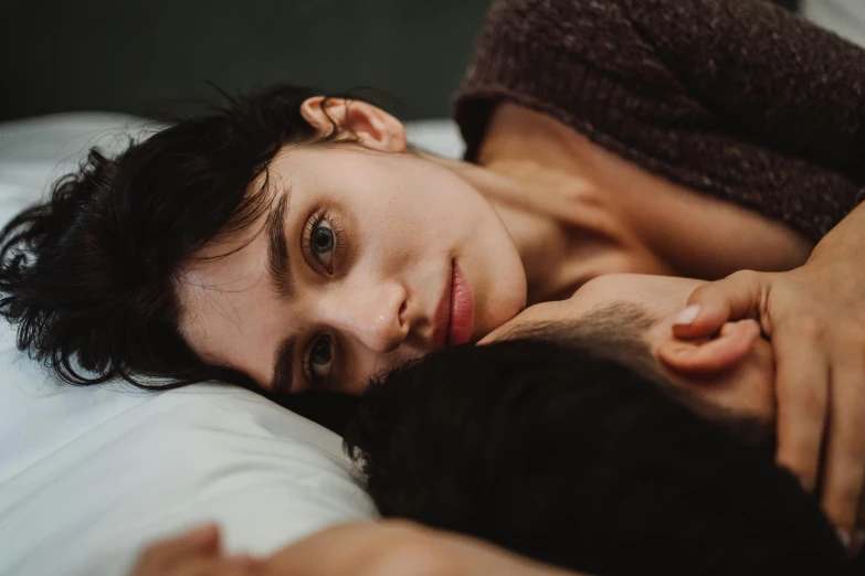 a person laying on a bed with his arm around a dog