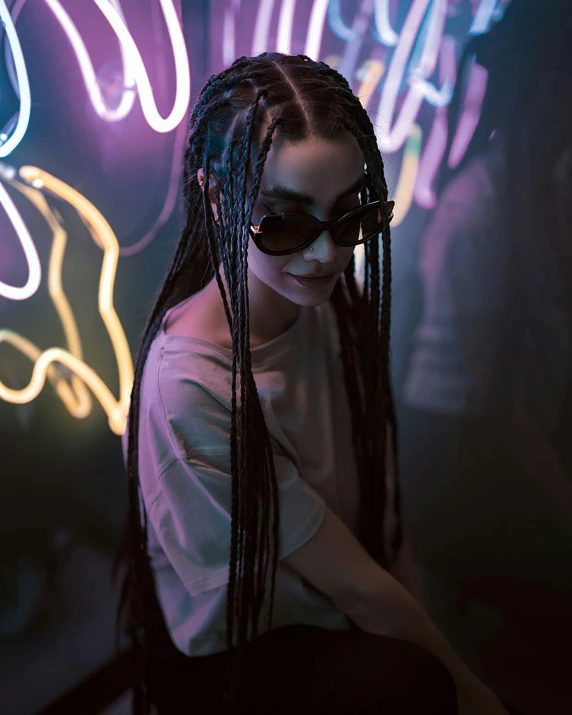 a woman sitting in front of neon lights with a long dreadlocked hair