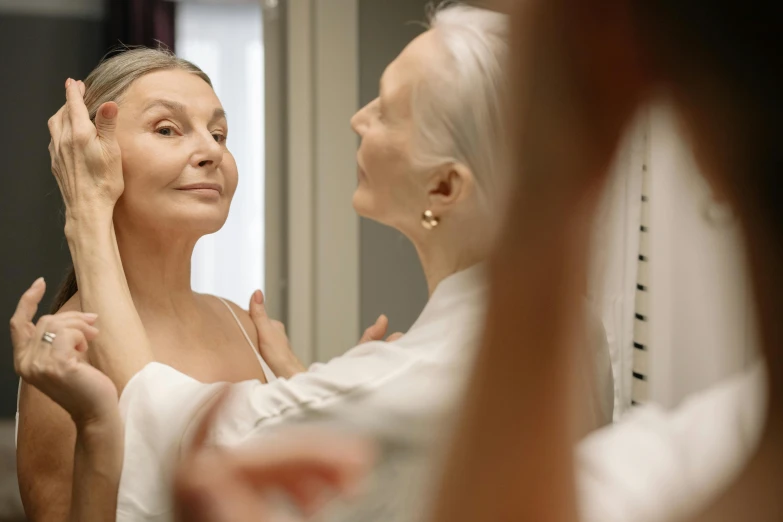 a woman combing her hair as the other looks on in the mirror