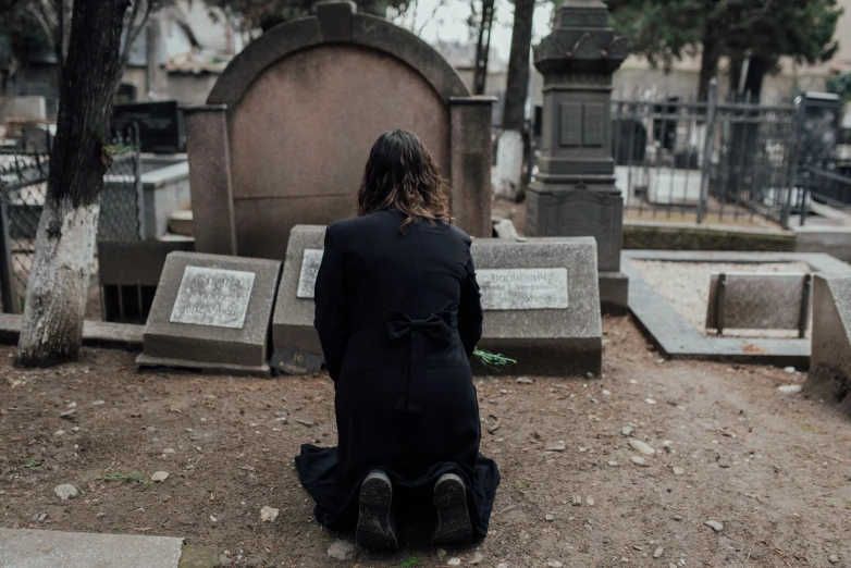 a woman is sitting on her knees in front of a cemetery