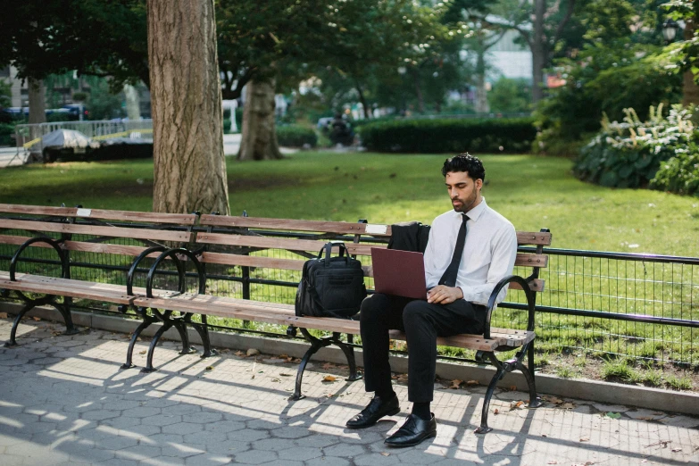 man with laptop sitting on a bench outside