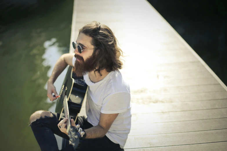 a bearded man with a skateboard sitting on a dock