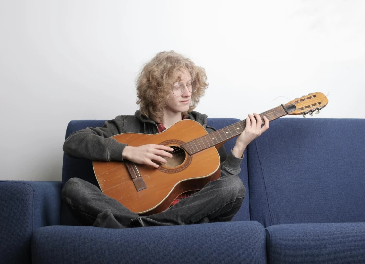 a young man sitting on a blue couch holding a guitar