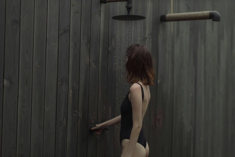 a woman in black bathing suit standing next to a wood wall