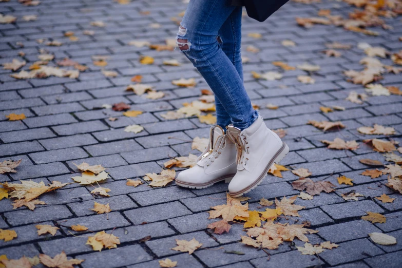 someone in a blue jacket and jeans is standing on a cobblestone path with yellow leaves