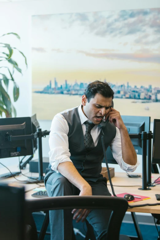 a man in business attire sitting at a desk while on the phone