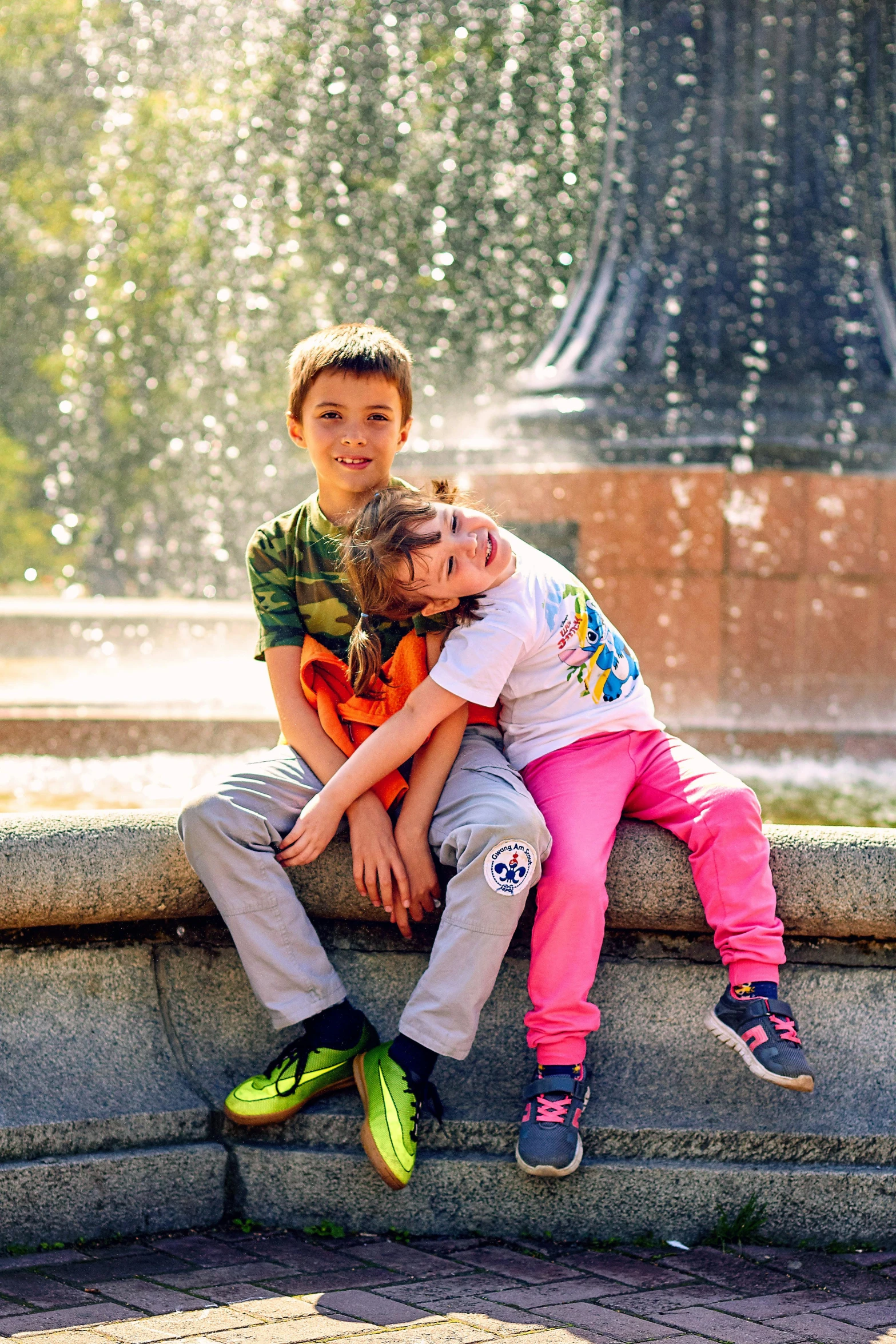 two children play on a ledge near a water fountain