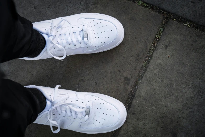 a person wearing white tennis shoes stands on a sidewalk