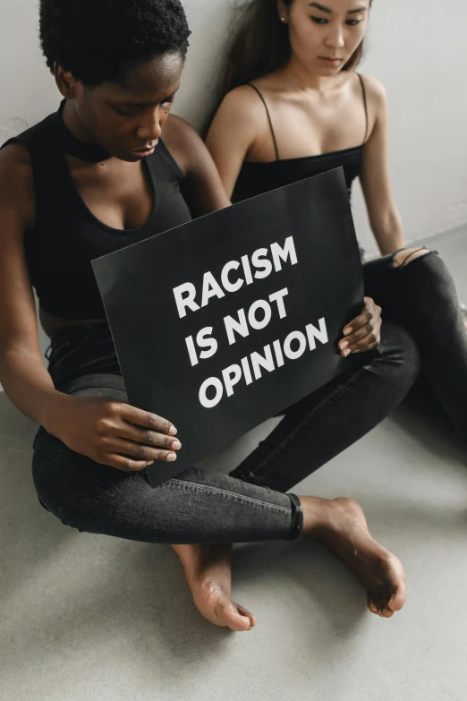 two women hold a sign against racism while they sit on the floor