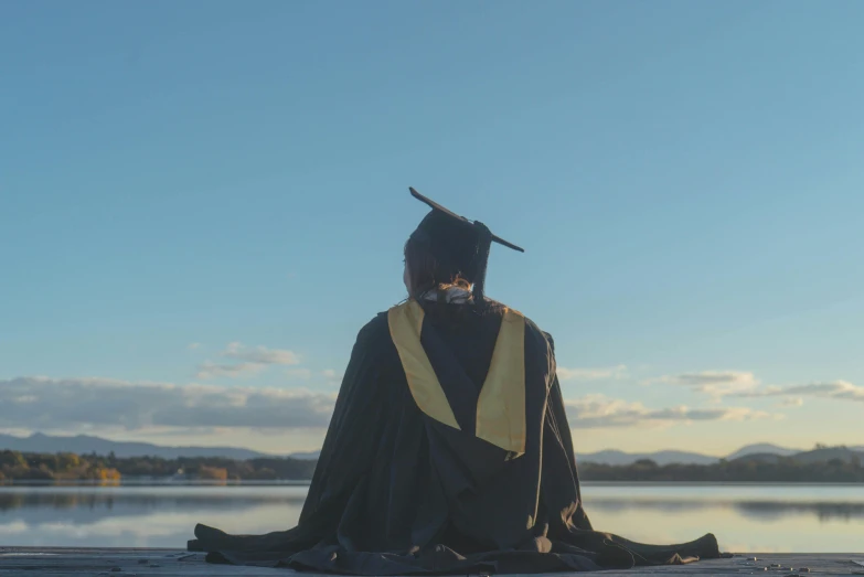 a man with a tassel and a graduation cap sits near a lake