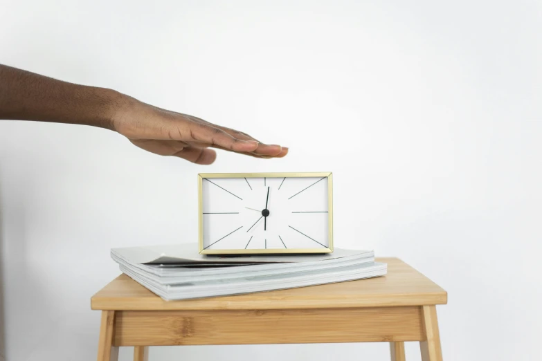 hand reaching for a small clock on top of some papers