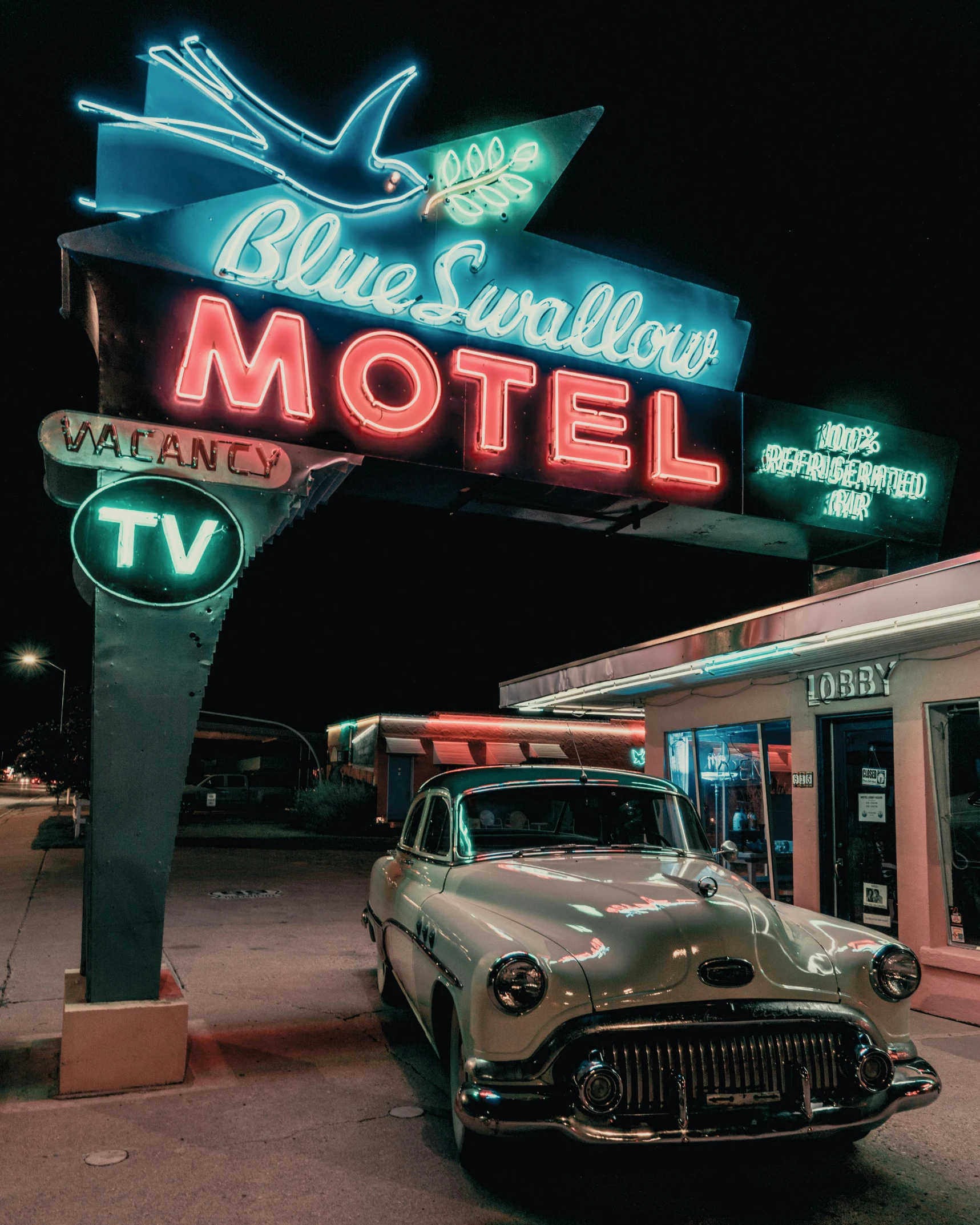 an old car parked outside a motel sign at night