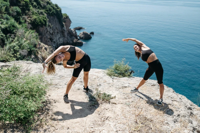 a man and woman are performing yoga on rocks near the ocean